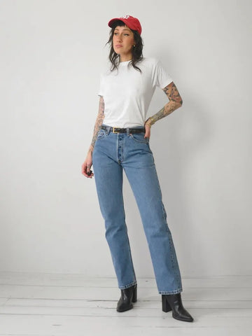 A person wearing a white t-shirt and the Classic 501 Levi's Jeans in a faded wash. They are also wearing a red cap, black boots, and have tattoos on their arms.